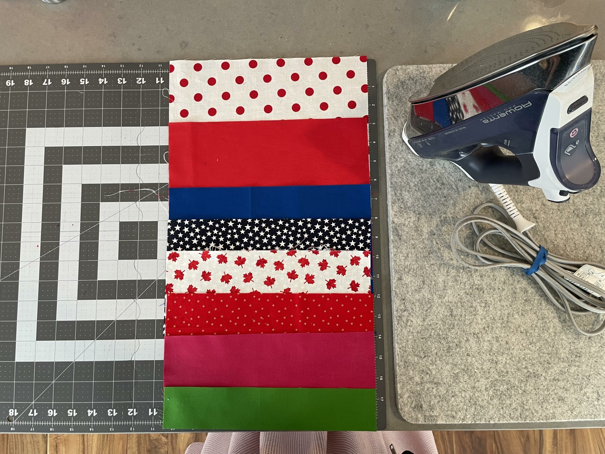 A column of cut fabrics representing countries winning gold medals are laid out on a cutting mat, waiting to be sewn