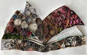 An open book with pages filled in by multicolored paper coils (pink, green, white, purple, yellow, burgundy, light blue, black, scarlet, and dark blue). The paper coils in the spine are pinched into different shapes while the ones in the pages are circular