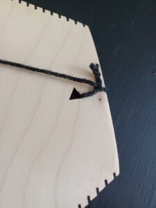 A close-up of the loom with thin black yarn tied into the triangle-shaped slot near the edge.