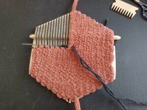 The same thin, black yarn is now being woven into the thick, rust-coloured yarn and across the remaining warp strands in the top left corner of the loom.