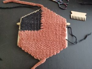 The weave is now complete, with thick, rust-coloured yarn taking up approximately 77% of the loom and thin, black yarn taking up the top left corner 24%. The loom comb and purple yarn scissors sit next to the loom.