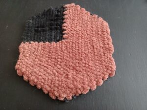 The completed weave now has black braille characters sewn in to the black woven section in the top left corner. The camera is angled on a tilt so the braille dots are visible.