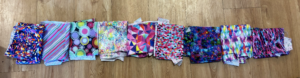 Nine rectangles of colorful, wild-patterned fabric sit in a row on a plain background.
