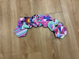 A handful of fun-patterned fabric hexagons sit on a plain surface. They are not yet stitched together.